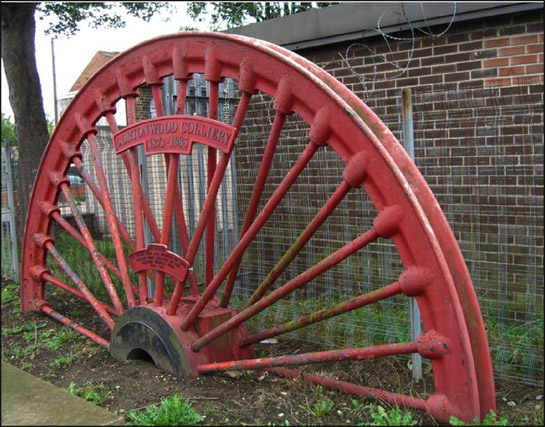 Figure 1:  Pit winding wheels are often set as memorials to both killed workers and former collieries in these communities.  This example, from Cortonwood Colliery, is adjacent to Brampton’s war memorial.